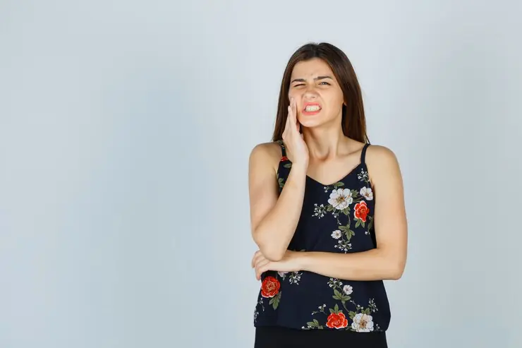 Woman grimacing, holding her cheek.